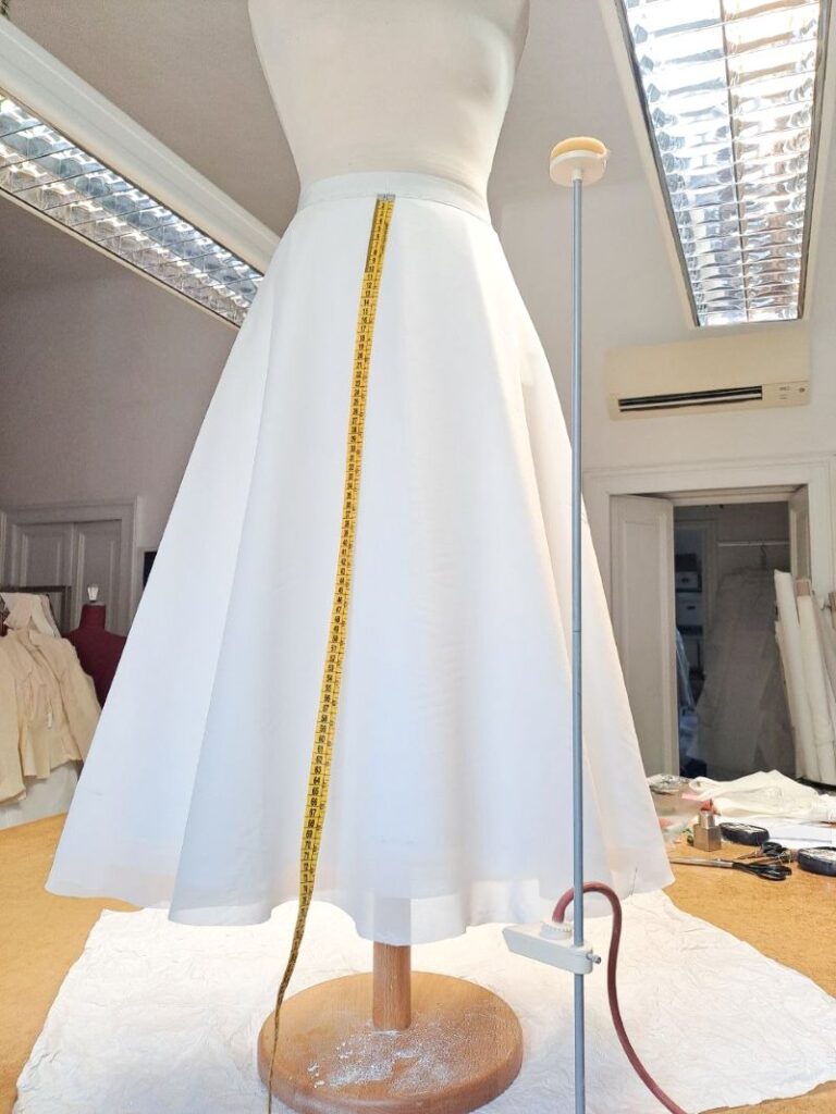 Controllo della lunghezza dell'orlo di una gonna da sposa su misura durante la lavorazione sartoriale