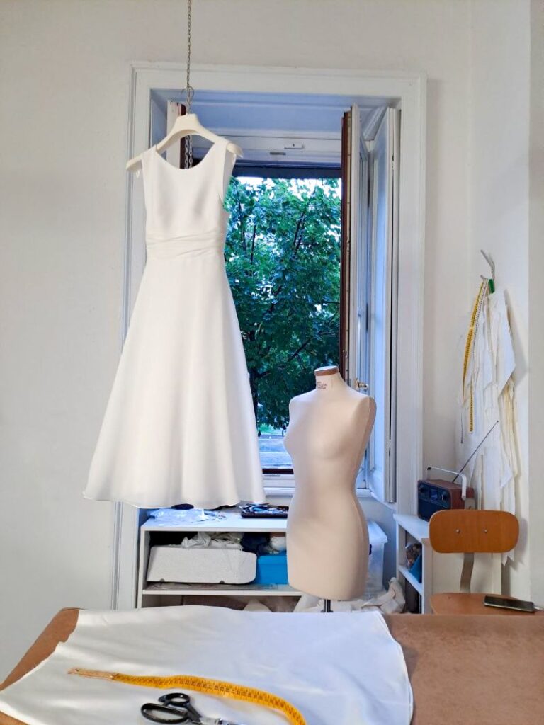 gonna sartoriale da sposa appesa in atelier durante le ultime fasi della lavorazione