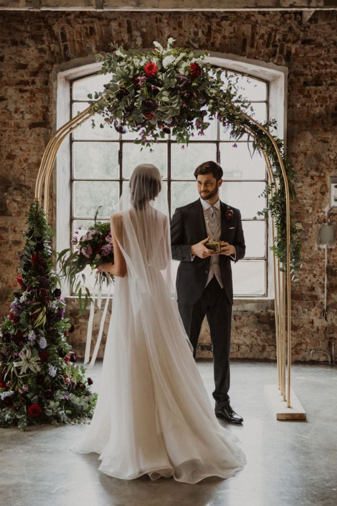 Sposa con velo davanti ad arco floreale in una fabbrica recuperata
