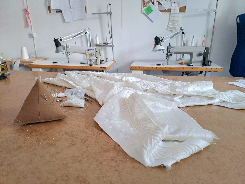 Laboratorio Talea Couture a Milano con macchine da cucire industriali e tessuti per abiti da sposa sul tavolo di lavoro